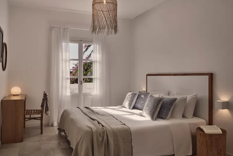 Une chambre lumineuse avec un grand lit et une fenêtre donnant sur une végétation luxuriante.