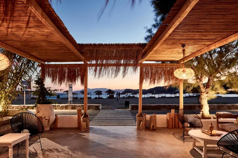Terrasse ombragée donnant sur une plage au coucher du soleil.