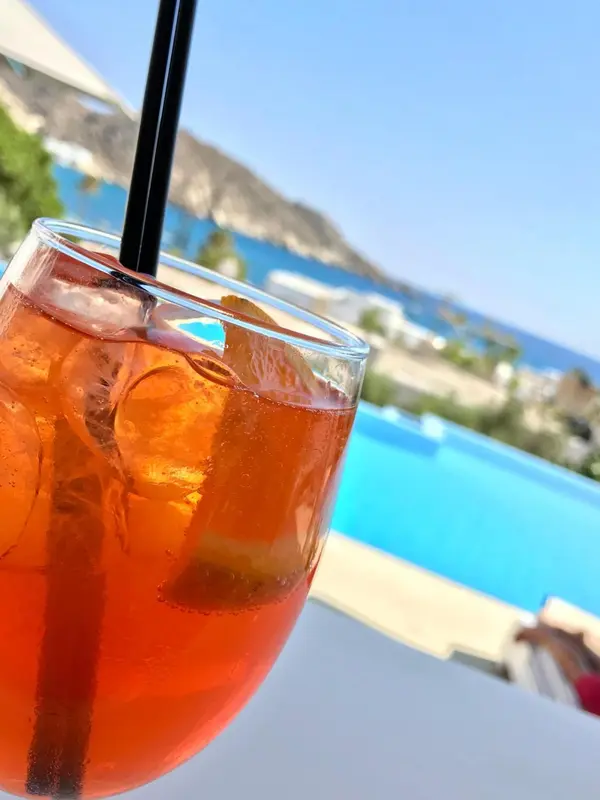 Un cocktail rafraîchissant avec des glaçons et une tranche d'orange, servi au bord d'une piscine turquoise.