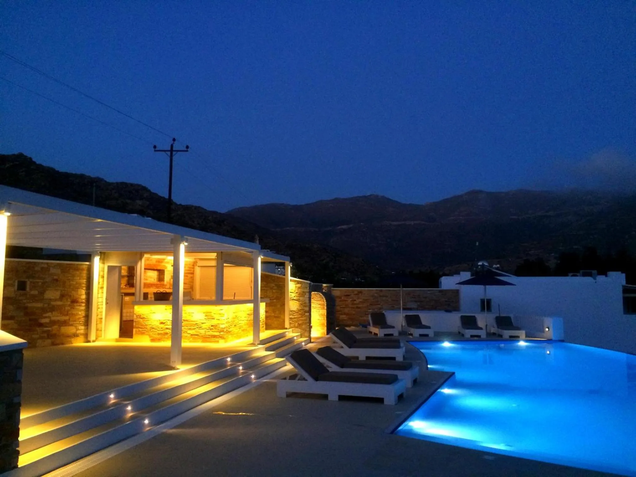 Terrasse lumineuse donnant sur une piscine éclairée et des montagnes au loin.