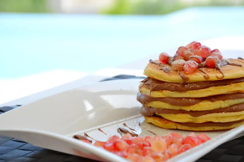 Une pile de crêpes nappées de chocolat et garnies de fruits rouges est présentée sur une assiette blanche.