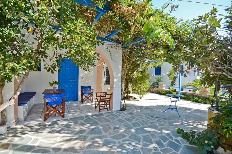 Terrasse ombragée avec mobilier bleu et blanc devant un bâtiment blanc.