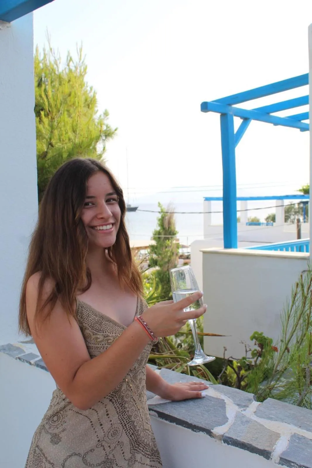 Une jeune femme tient un verre sur une terrasse ensoleillée avec vue sur la mer.