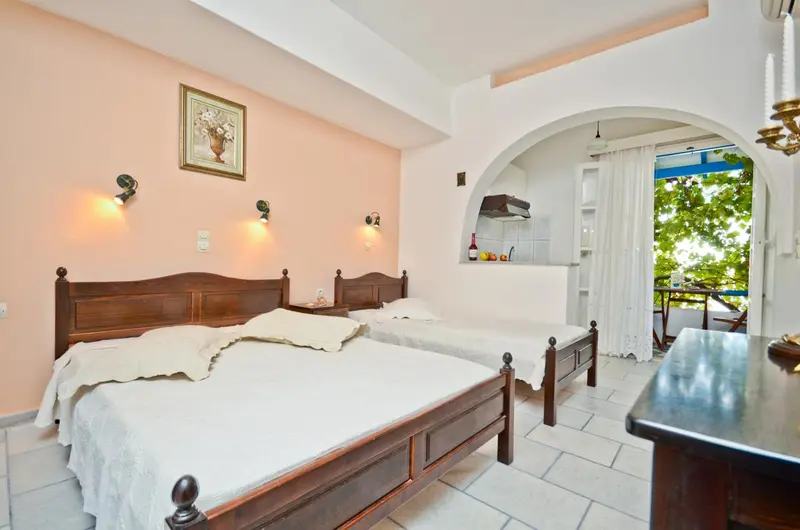Une chambre lumineuse avec deux lits simples et une kitchenette en fond.