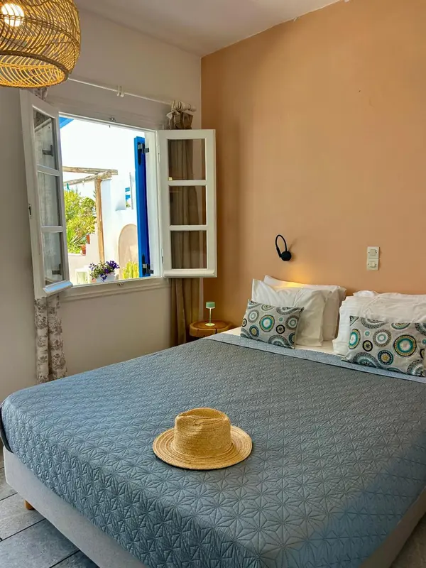 Une chambre lumineuse avec un lit recouvert d'une courtepointe et un chapeau de paille posé sur le couvre-lit.