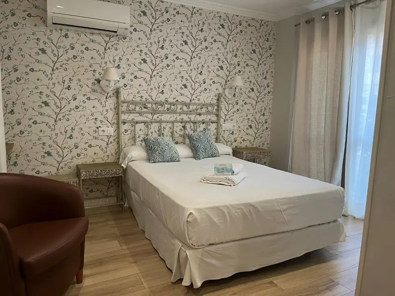 Une chambre lumineuse avec un lit double et un fauteuil.