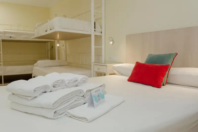 Lits superposés et lit simple avec linge de lit blanc et oreillers colorés dans une chambre lumineuse.