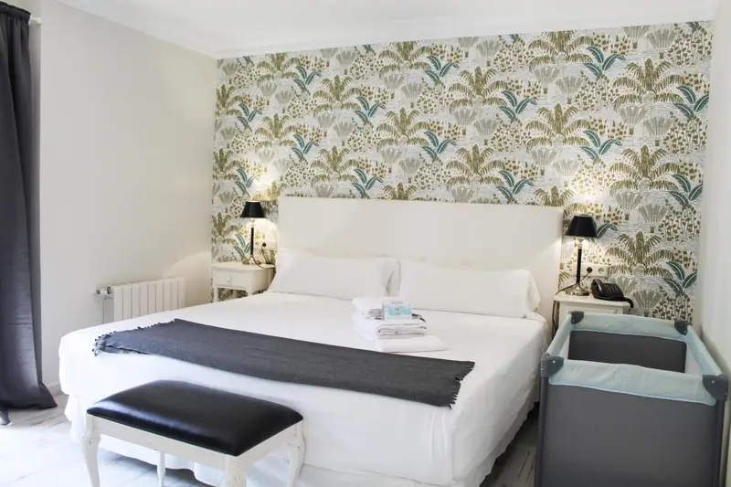 Une chambre lumineuse avec un grand lit recouvert d'une couverture sombre et de coussins blancs.