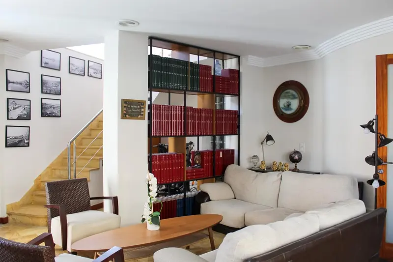Un salon clair avec canapés, fauteuils et une bibliothèque décorative.