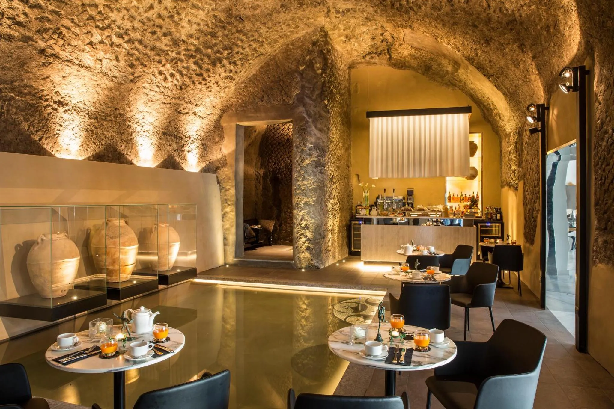 Une salle voûtée éclairée présente des tables dressées pour le petit-déjeuner.