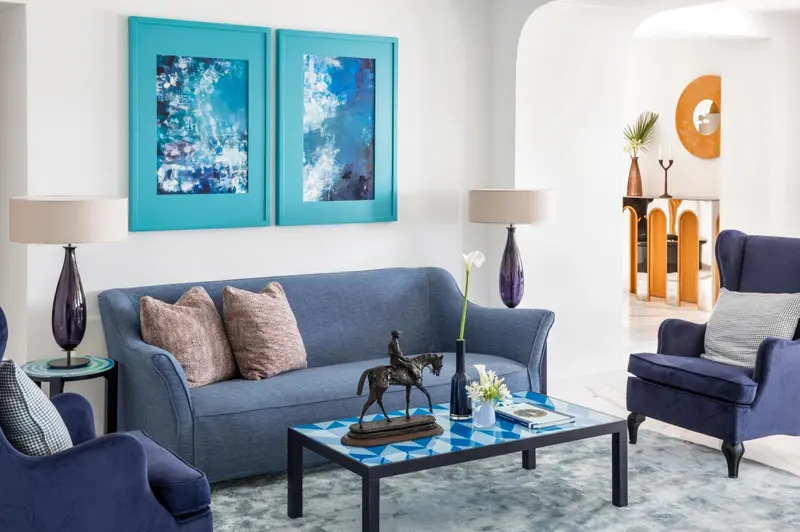 Un salon bleu et gris avec des œuvres d'art murales et des lampes.
