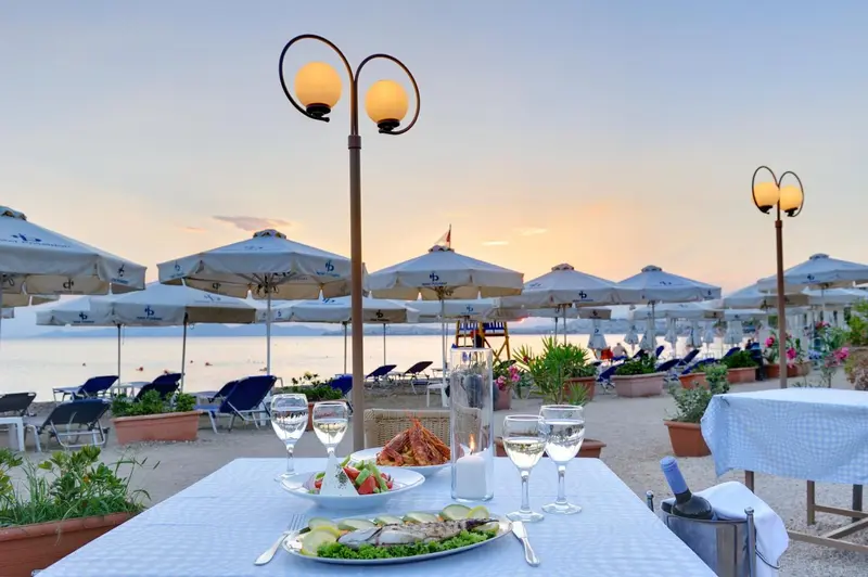 Une table dressée avec des plats de fruits de mer face à la mer au coucher du soleil.
