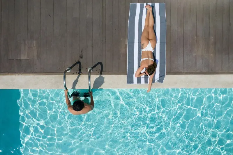 Vue aérienne d'une piscine avec deux personnes se relaxant au soleil.