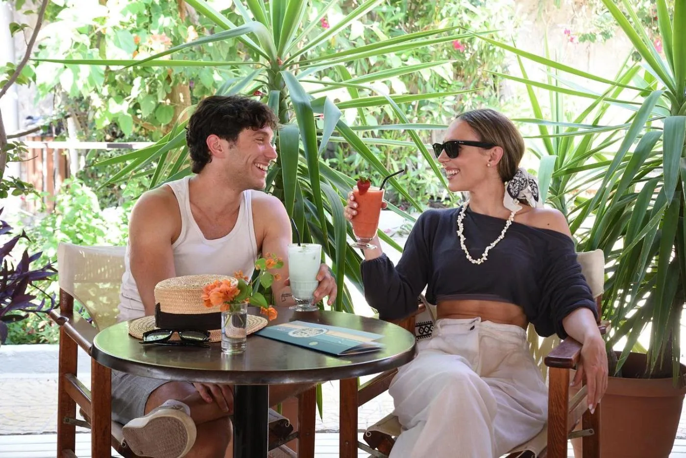 Un couple souriant est assis à une table en terrasse, avec des boissons colorées.