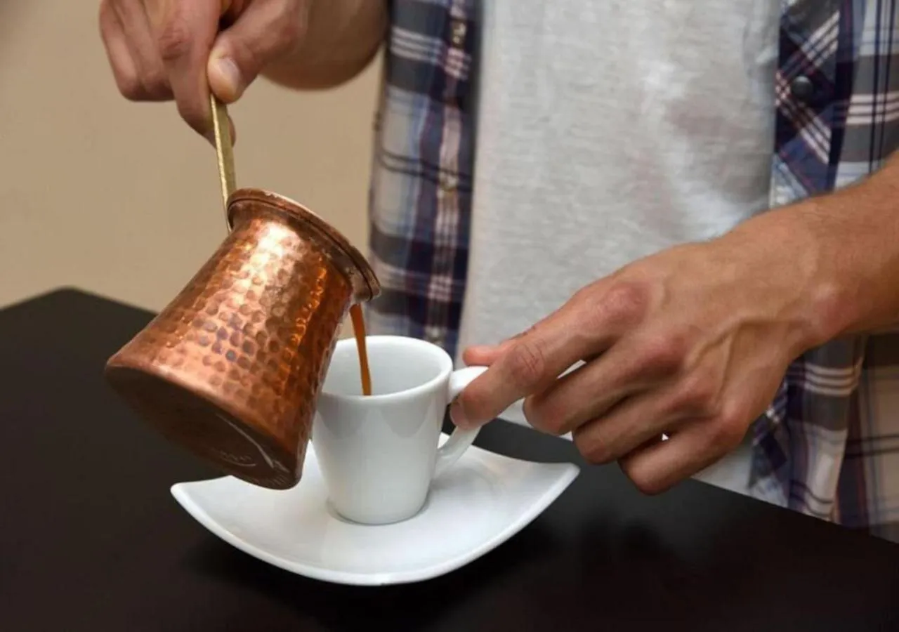 Une personne verse du café dans une tasse blanche.