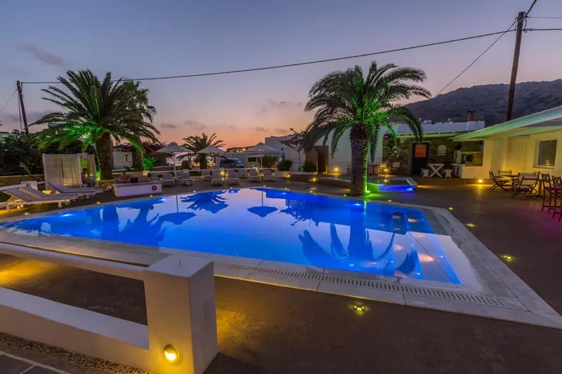 Piscine illuminée avec chaises longues et végétation tropicale au crépuscule.