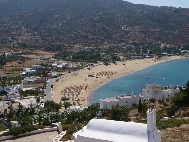 Vue aérienne d'une plage de sable fin bordée d'eau turquoise et de bâtiments blancs.
