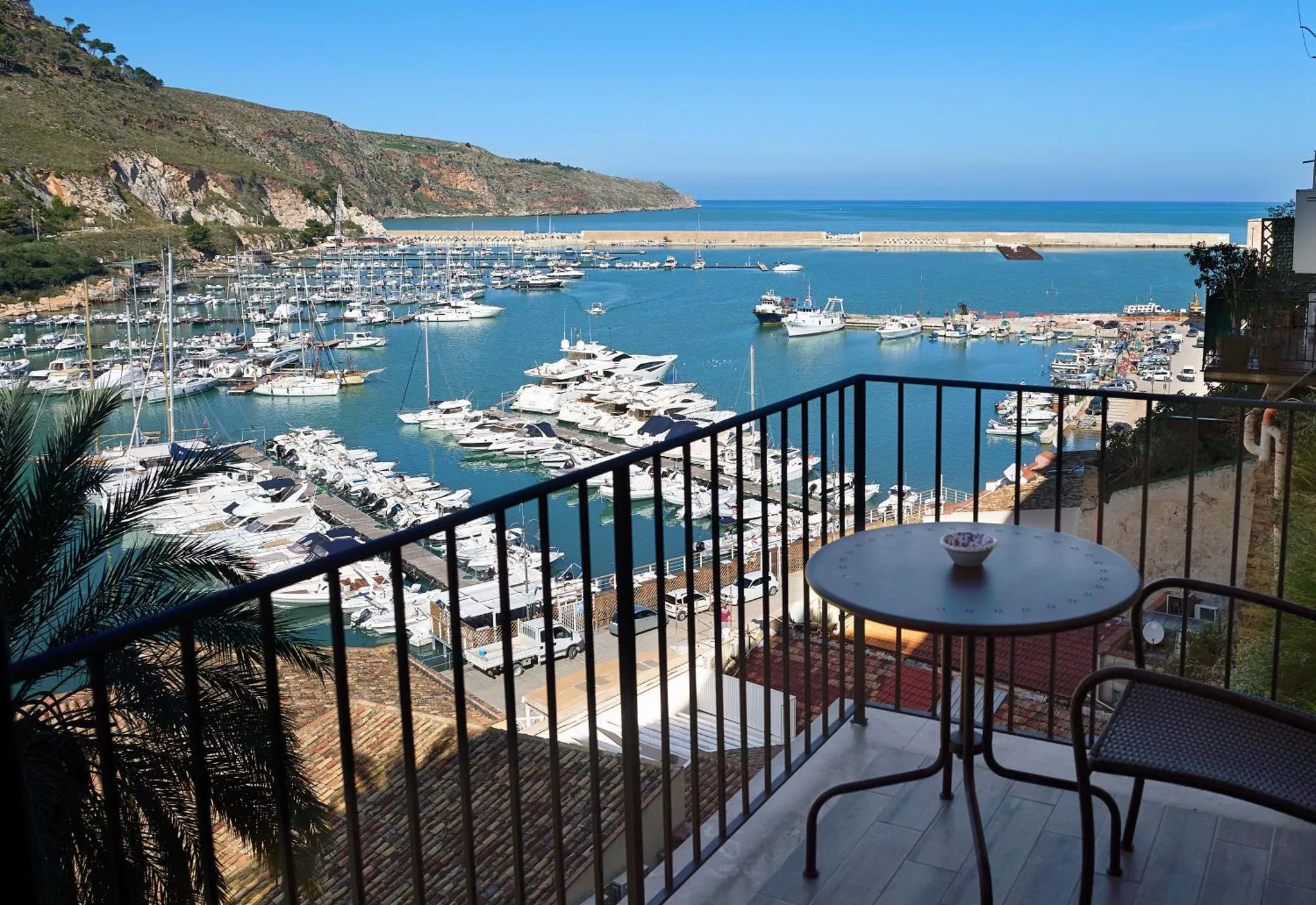 Vue d'une terrasse avec table et chaises donnant sur un port de plaisance ensoleillé.