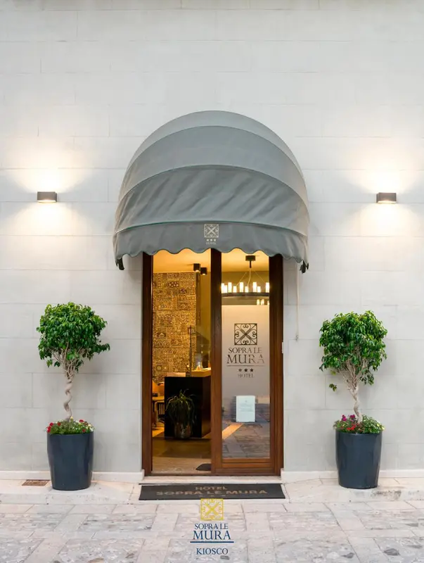 Entree d'un hotel avec auvent et pots de plantes.