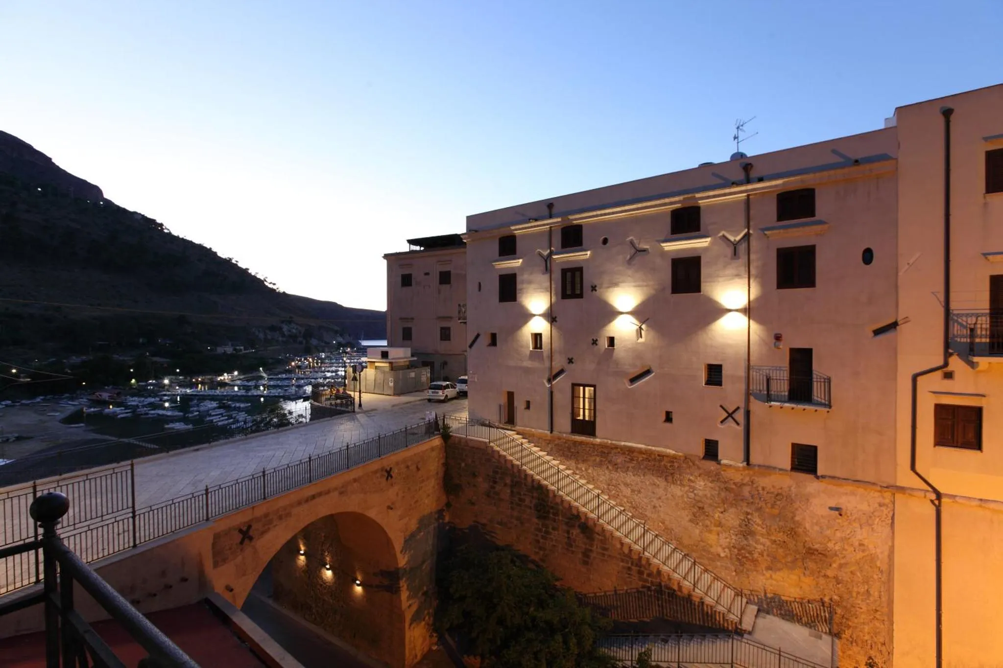 Bâtiment clair avec des fenêtres et des balcons, surplombant une ville côtière au crépuscule.