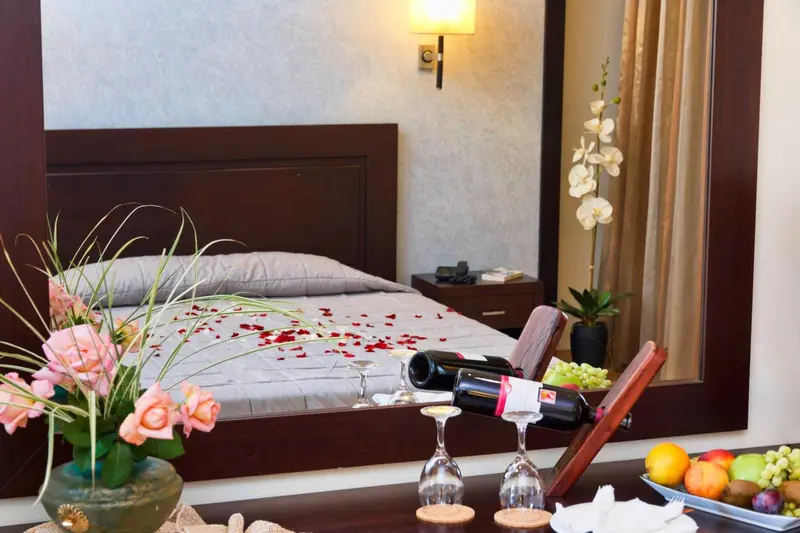 Une chambre décorée avec un lit recouvert de pétales de fleurs et une bouteille de vin.