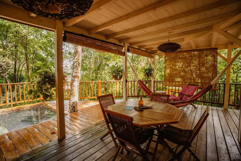 Terrasse en bois avec table, chaises et hamacs dans un cadre tropical.