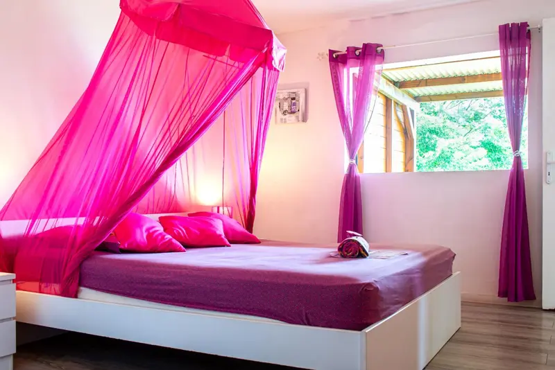 Une chambre lumineuse avec un lit recouvert d'une moustiquaire rose et de coussins violets.