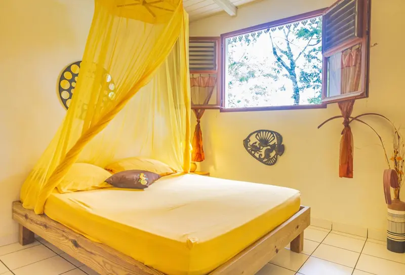 Une chambre lumineuse avec un lit recouvert d'une moustiquaire jaune.