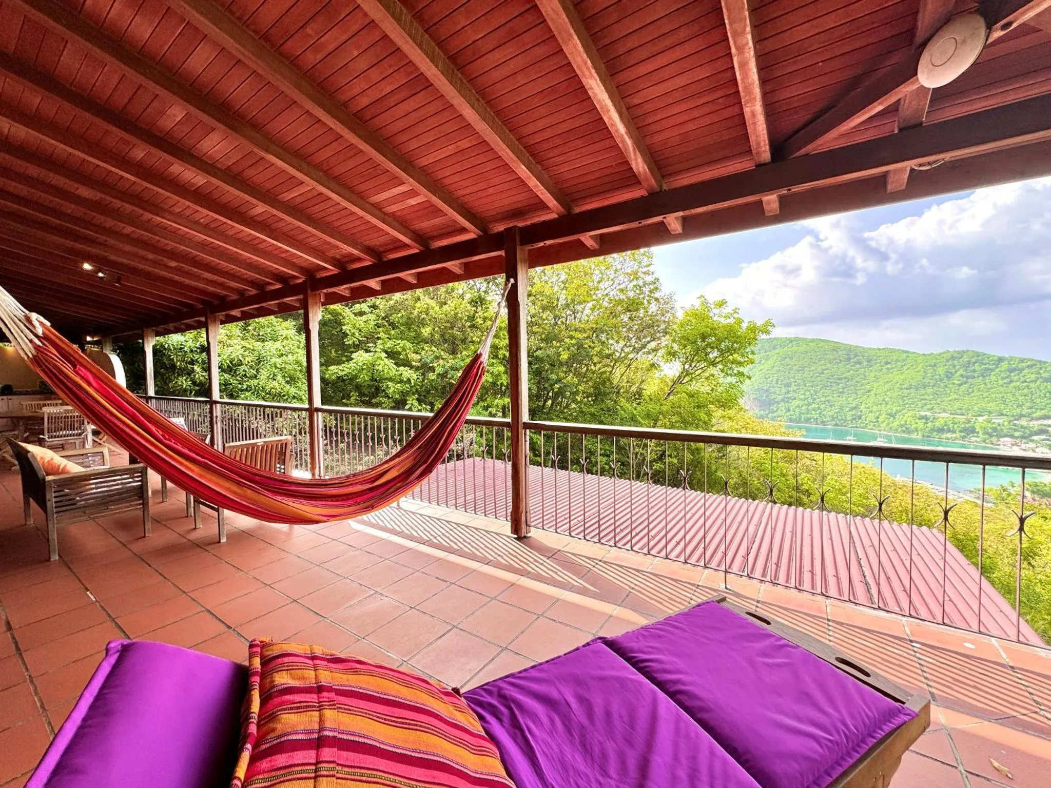 Terrasse ombragée avec hamac et vue sur la végétation et la mer.