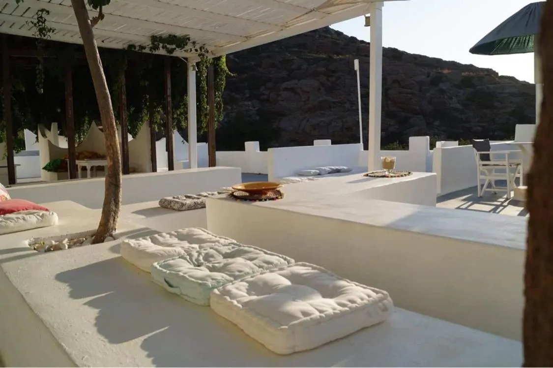 Espace de détente extérieur avec coussins et pergola ombragée.
