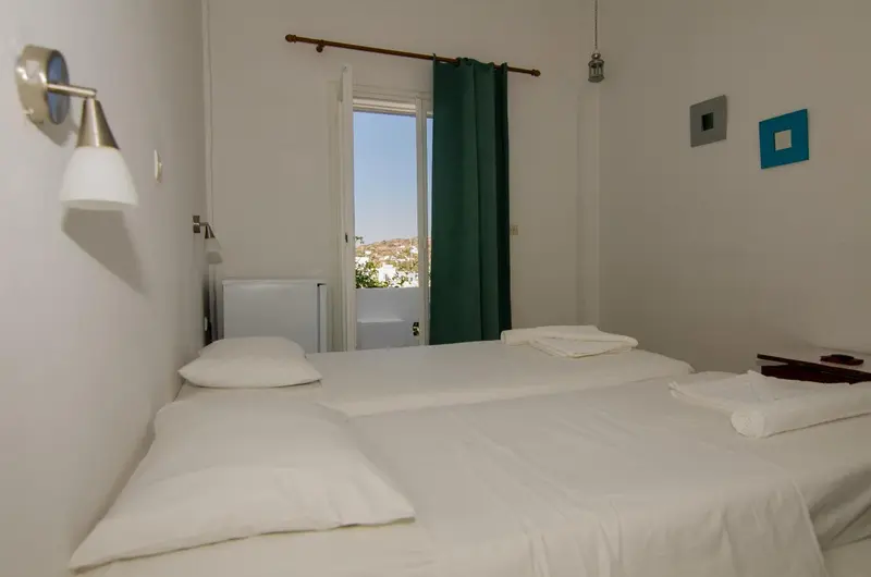Une chambre lumineuse avec deux lits simples et une fenêtre ouverte sur un paysage urbain.