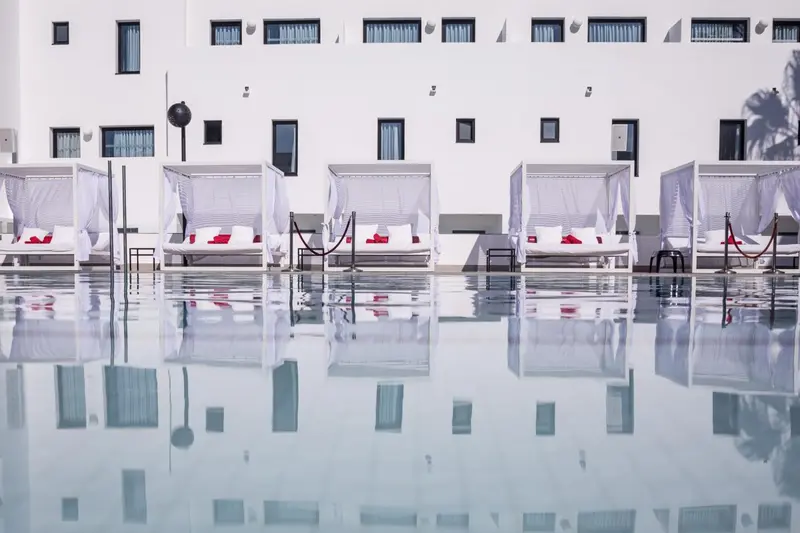 Transats blancs et coussins rouges disposés au bord d'une piscine à eau claire.