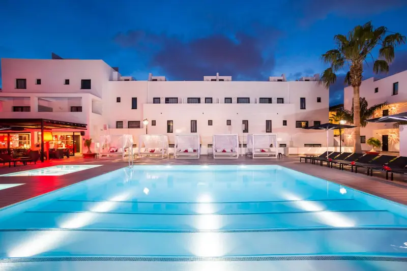 Bâtiment blanc illuminé avec piscine et mobilier de détente.