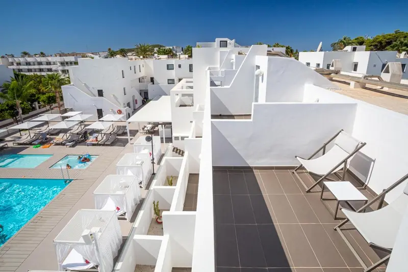 Terrasse avec transats et piscine au premier plan, bâtiments blancs en arrière-plan.