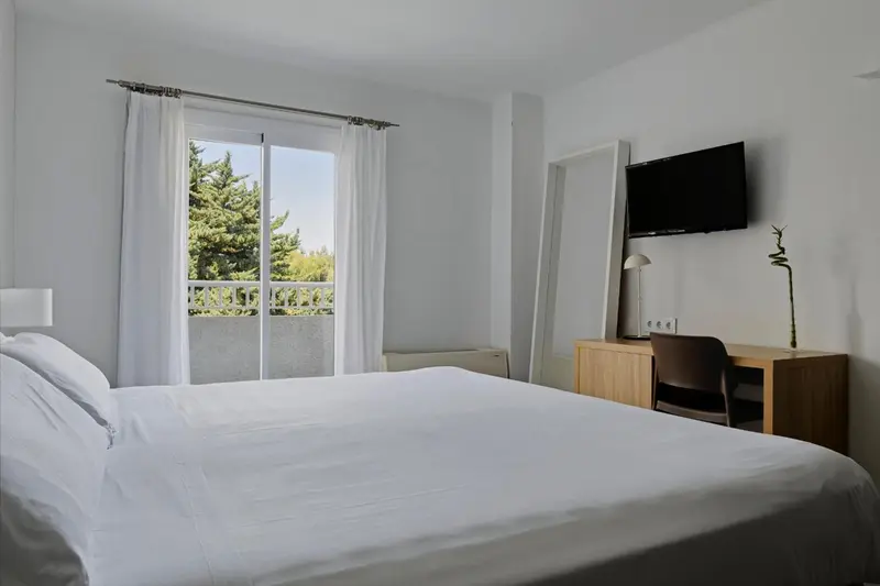 Une chambre lumineuse avec un grand lit et un bureau près d'une baie vitrée.