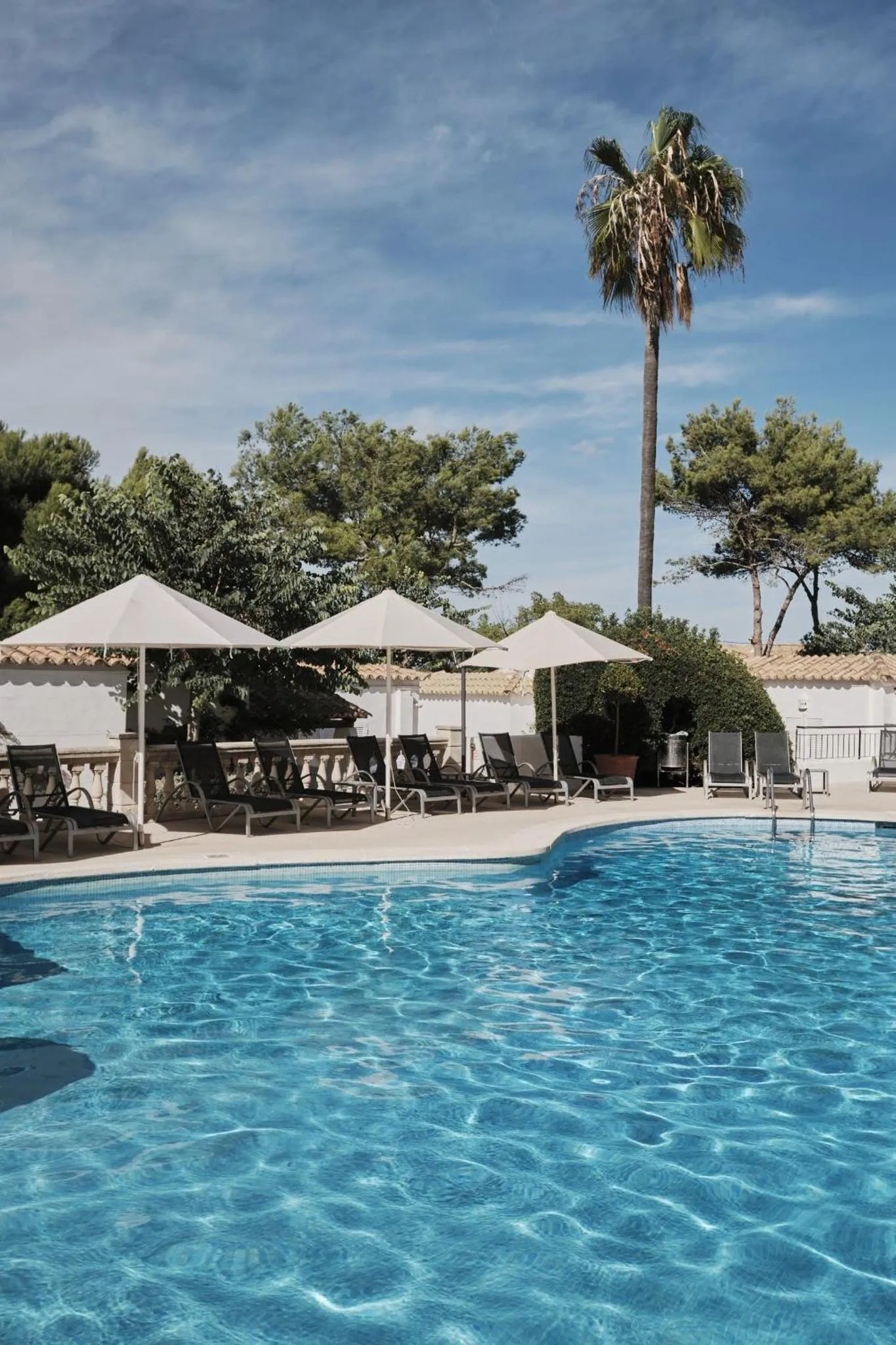 Transats et parasols bordent une piscine bleu clair sous un ciel dégagé.
