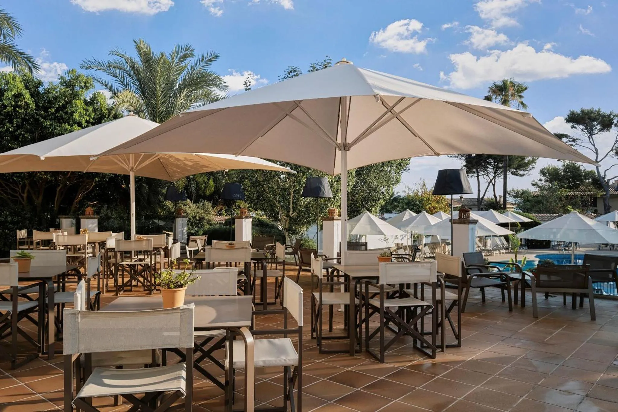 Terrasse ombragée avec tables et chaises disposées sur un sol carrelé.