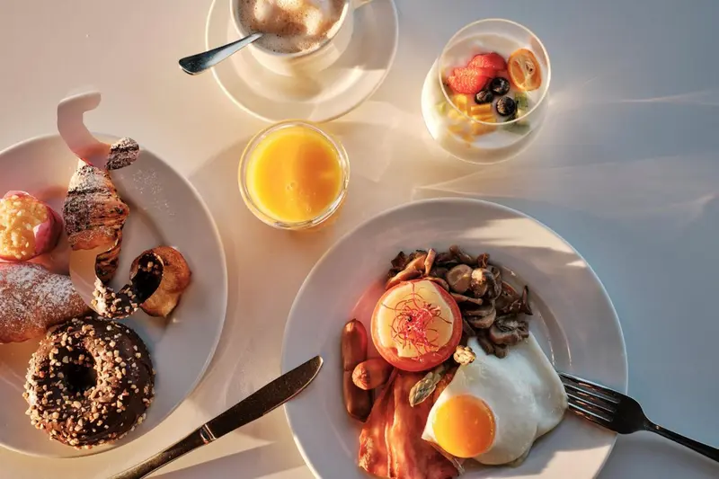 Une table est dressée avec un petit-déjeuner composé de viennoiseries, de fruits et d'une assiette salée.