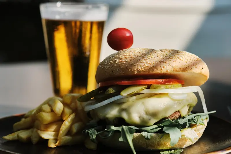 Un hamburger garni et un verre de bière sont servis avec des frites.