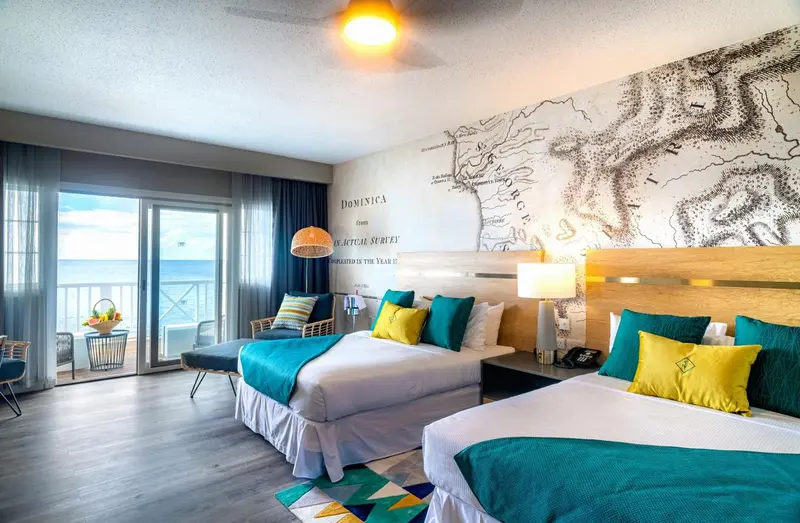 Chambre lumineuse avec deux lits et vue sur la mer par de grandes baies vitrées.
