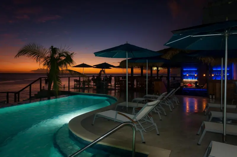 Terrasse avec piscine illuminée et bar en arrière-plan au coucher du soleil.