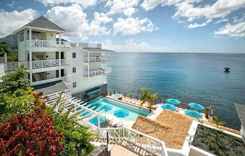 Vue d'un bâtiment blanc avec des balcons surplombant une piscine et la mer.