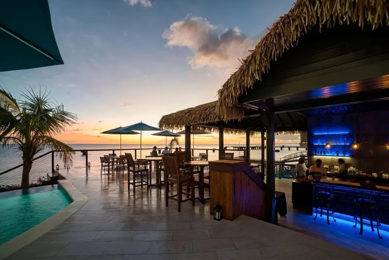 Terrasse avec bar et piscine face à la mer au coucher du soleil.