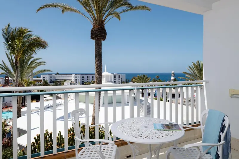 Une terrasse avec une table et des chaises offre une vue sur la mer et la végétation.