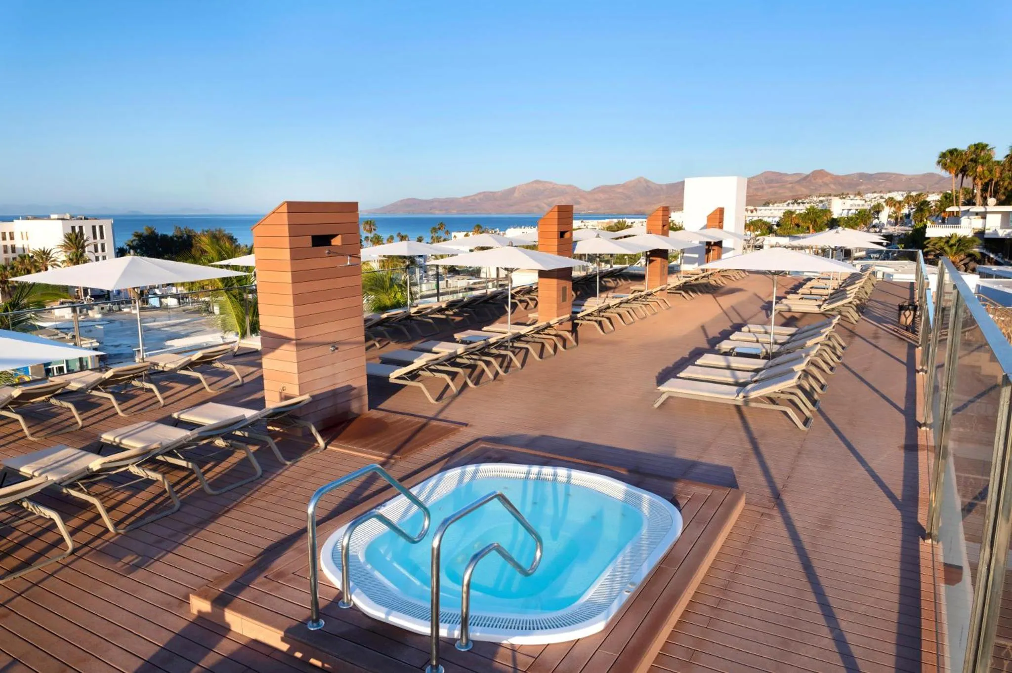 Terrasse avec transats et jacuzzi offrant une vue sur la mer et les montagnes.