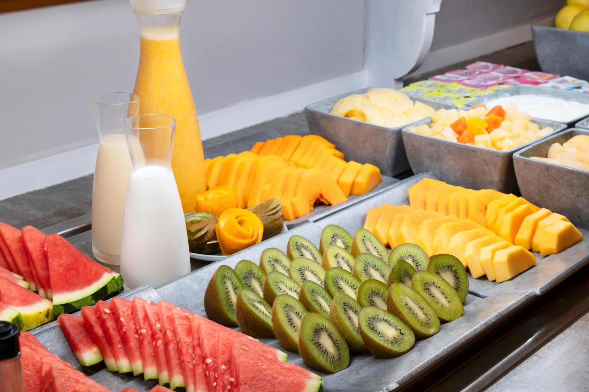 Un buffet propose des fruits frais coupés et du jus.