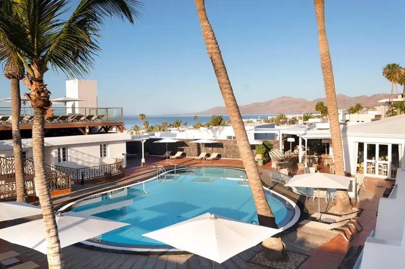 Une piscine rectangulaire avec des transats et des parasols, entourée de végétation et donnant sur la mer.