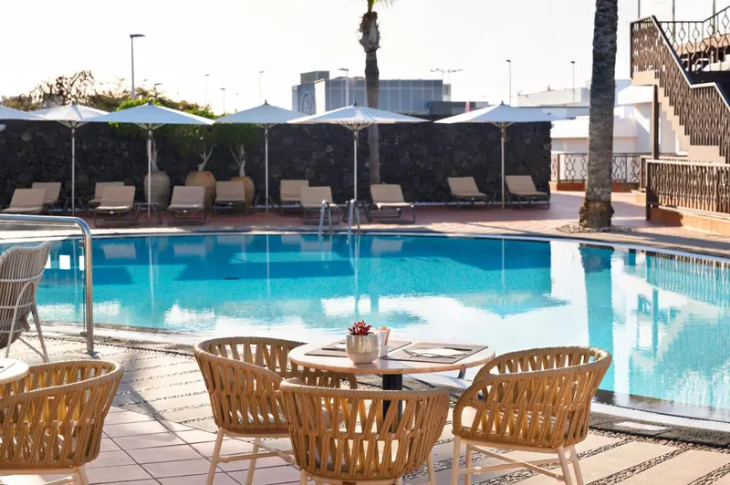 Transats et tables de jardin au bord d'une piscine ensoleillée.