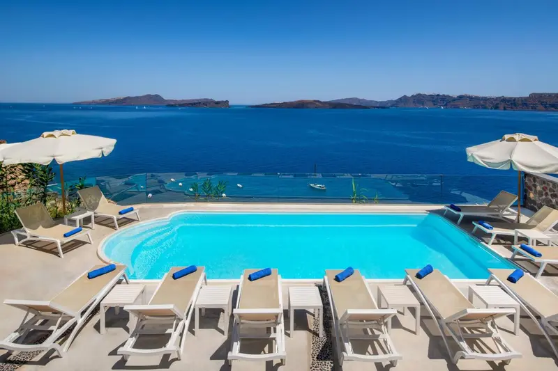 Transats blancs alignés au bord d'une piscine turquoise avec vue sur la mer et les îles au loin.