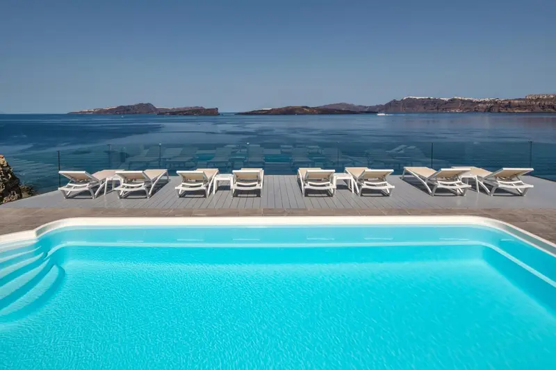 Transats blancs alignés au bord d'une piscine turquoise avec vue sur la mer et des îles au loin.